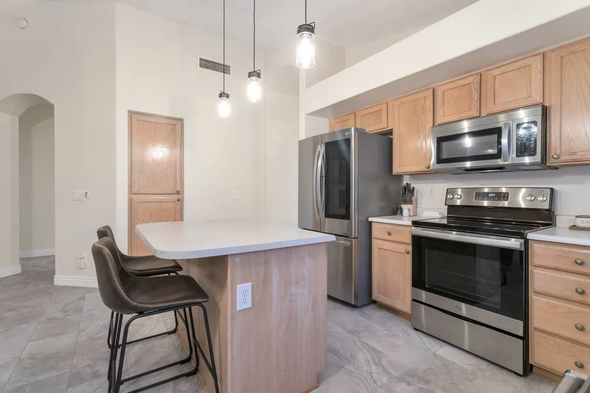 A bright, modern kitchen with a spacious island takes center stage. Stainless steel appliances, including a double-door refrigerator and oven, gleam under pendant lighting. Ample countertops and seating suggest a space perfect for both meal prep and socializing, while the open layout visually connects the kitchen to adjacent living areas.