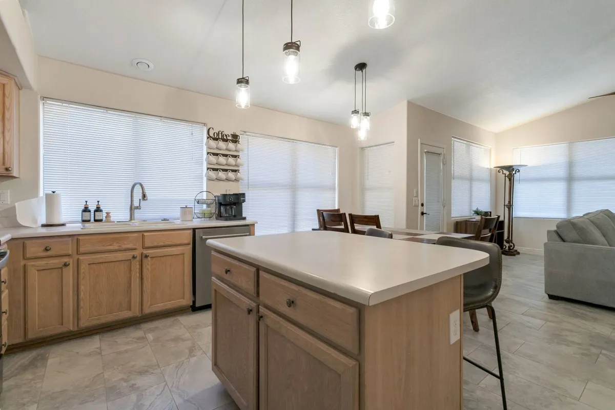 A view from the kitchen island reveals a dedicated coffee station with both Keurig and traditional coffee makers. The adjoining dining area is clearly visible, suggesting seamless movement between spaces for family gatherings and casual meals. Warm lighting and inviting decor enhance the sense of home-cooked comfort.