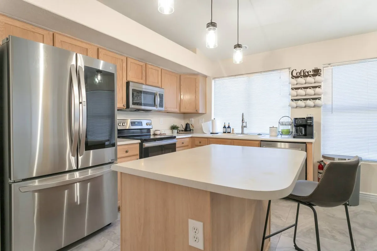 The kitchen features modern stainless steel appliances, a generous island for prep or seating, and a large window that fills the space with natural light. The open plan hints at easy flow between the kitchen and other living areas, inviting social interaction during meal times.