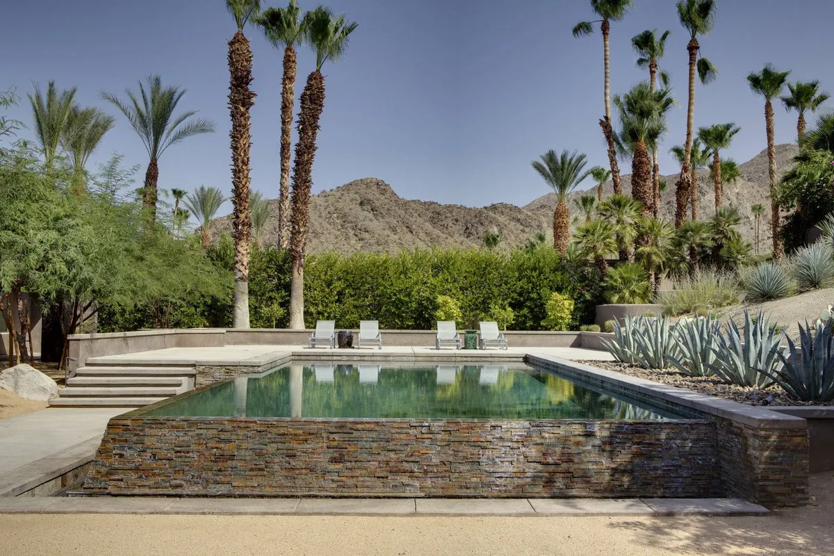 This exterior image showcases a sparkling swimming pool surrounded by palm trees and lounge chairs, all set before a scenic mountain backdrop. The inviting pool area suggests a relaxing and social atmosphere, perfect for gatherings and unwinding after exciting local events.