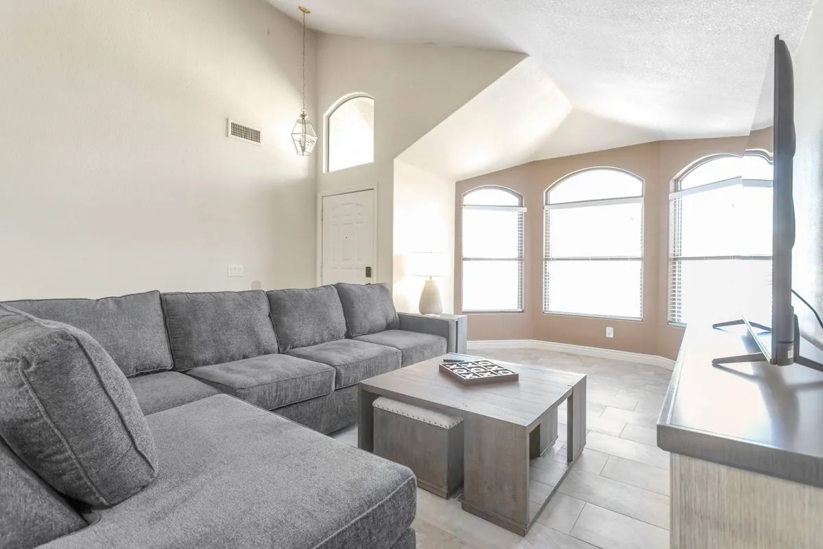 This image captures a spacious living area filled with natural light, featuring a large plush sectional sofa and a coffee table. The window lets in abundant sunlight, creating a cozy atmosphere perfect for relaxation and socializing. The setup is inviting for gatherings, morning coffee, or movie nights.