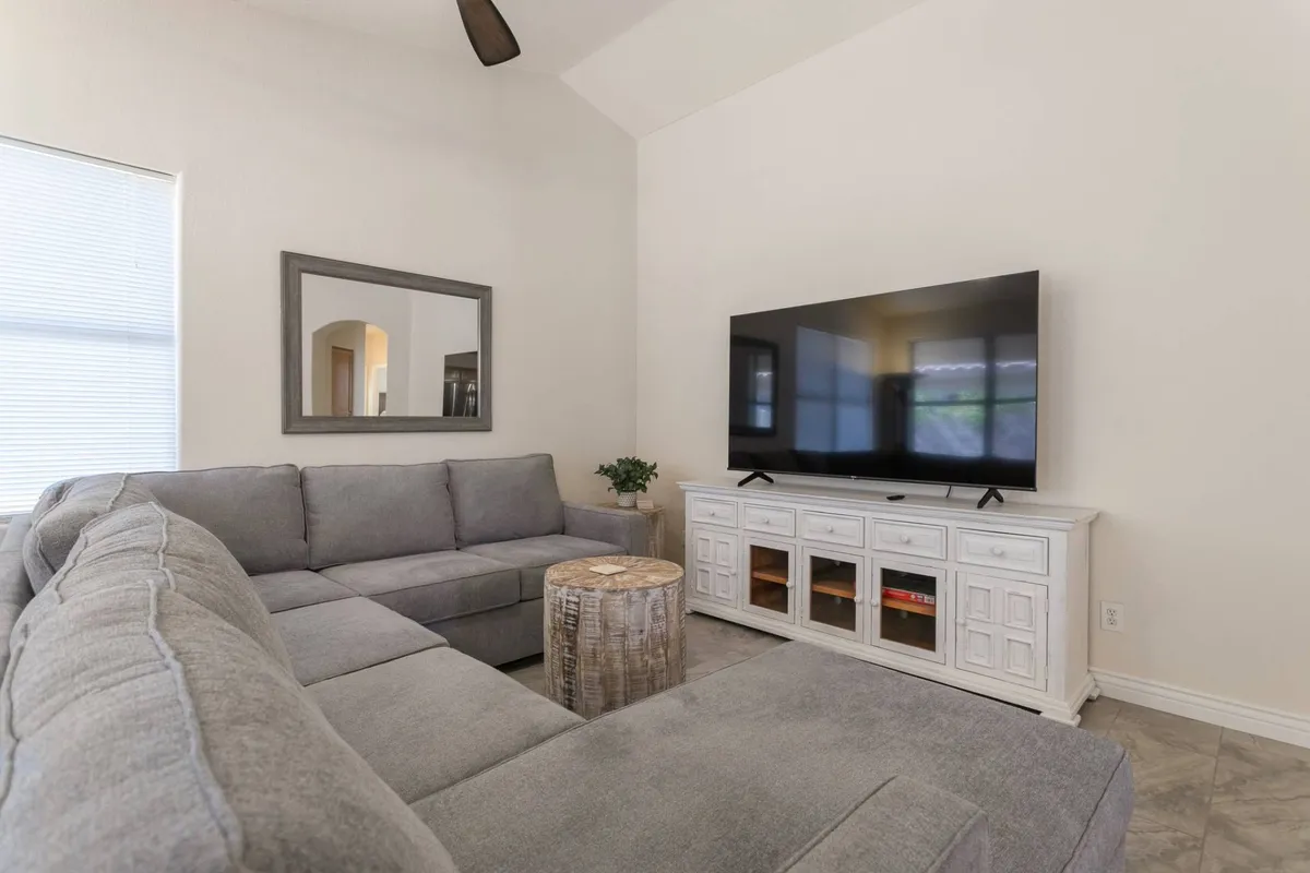 This image showcases a comfortable living room with a sectional sofa, television, decorative mirror, and a coffee table. The area is arranged to foster conversation and relaxation, and the TV is positioned perfectly for group movie nights or catching the game together.